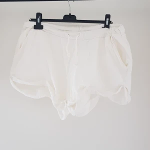 Vita shorts med snörning från H&M strl L - Supermjuka vita shorts från H&M Basic i frotté med elastisk midja och snörning framtill. De har en loose passform och två sidofickor, perfekta för chill dagar eller strandhäng. Lätta att matcha med allt och riktigt sköna att bära under varma sommardagar.  Mudden har "krulllat" ihop sig & små noppror annars helt skick