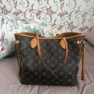 Louis Vuitton Neverfull monogramväska - Säljer en klassisk Louis Vuitton Neverfull med ikoniskt monogrammönster i brunt och beige. Väskan har läderdetaljer, långa handtag och rymligt fack med innerficka. Perfekt för dig som vill ha en lyxig och tidlös axelväska med plats för allt du behöver. Jag kan gå med på att förhandla priset 