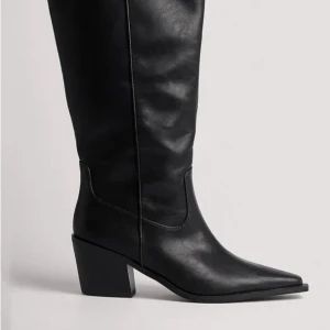 Svarta cowboy boots i skinn - Snygga svarta cowboy boots med spetsig tå och bred klack. Skorna är höga och tillverkade i skinn, vilket ger en cool och stilren look. Perfekta att matcha med kjol eller jeans för en trendig outfit.