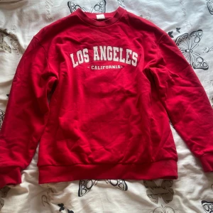 Röd sweatshirt från Stories  - Säljer denna röda sweatshirt från Stories i storlek M med trycket 'Los Angeles California' i vitt framtill. 