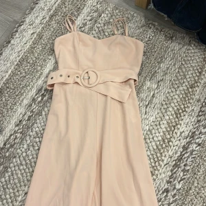 Korallrosa jumpsuit Gina Tricot - Supersnygg  jumpsuit från Gina Tricot med smala axelband och markerad midja med bälte och runt spänne. Klänningen har dragkedja där bak. Storlek 36