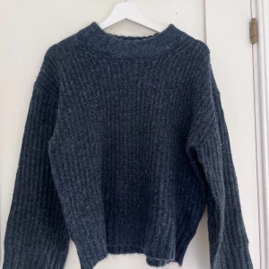 Mörkblå stickad tröja - Mysig mörkblå stickad tröja med grov ribbad struktur och högre rund hals. Tröjan är använd ett par gånger men är ändå i väldigt fint skick. Jag skulle säga att tröjan är lite större i storleken så passar personer med iallafall storlek XS/S