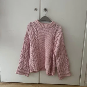 Rosa stickad tröja från Gina Tricot - Supermysig ljusrosa stickad tröja från Gina Tricot med grova flätstickade detaljer på ärmarna och sidorna. Tröjan har en rund halsringning, breda muddar och lång ärm. Perfekt för lager-på-lager under kyliga dagar.