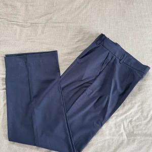 Mörkblå kostymbyxor Pull&Bear S - Snygga mörkblå kostymbyxor från Pull&Bear Black Label. Byxorna har raka, vida ben, hällor för bälte och  ficka bak. Perfekta för en clean och stilren look. Materialet är mjukt och följsamt, vilket gör dem bekväma hela dagen.