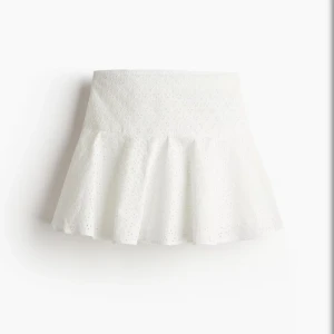 Vit broderad kortkjol från H&M - Superfin vit kortkjol från H&M med broderade blommor och lätt volang. Kjolen är i bomull och har en söt, somrig känsla med utsvängd form. Perfekt att styla med en crop top eller oversized skjorta för en fräsch look.