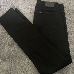 Svarta  jeans från Lee - Säljer ett par svarta jeans från Lee med klassisk femficksdesign och Lee-logga på bakfickan. Jeansen har smal passform och är tillverkade i mjukt bomullsmaterial med stretch för extra komfort. Hör av er vid frågor eller funderingar