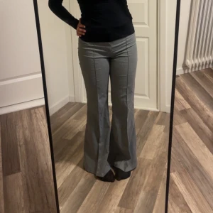 Grå bootcut kostymbyxor - Snygga grå kostymbyxor med bootcut passform och pressveck framtill. Byxorna har hög midja och sitter tajt över höfterna innan de släpper ut i ett vidare ben. Perfekta för dig som gillar en klassisk men trendig look.