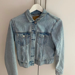 Ljusblå klassisk jeansjacka - Snygg ljusblå jeansjacka med klassisk passform och coola detaljer som bröstfickor med knappar och silverfärgade knappar framtill. Jackan har lång ärm och är tillverkad i slitstarkt denim. Perfekt att slänga över en hoodie eller t-shirt för en chill look.