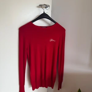 Röd långärmad tröja från Galvanni - Riktigt snygg röd långärmad tröja från Galvanni med glittrig logga framtill. Tröjan är i mjukt material med viskos, polyakryl och polyester. Enkel och stilren passform som funkar till många outfits. Perfekt för dig som gillar en clean look med lite extra bling.