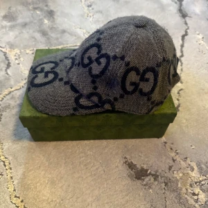 Gucci keps i grå denim med GG-mönster - Snygg keps från Gucci i grå wool med mörkblå GG-loggor över hela kepsen. Klassisk form med böjd skärm. Perfekt statement-piece för dig som gillar lyxiga accessoarer och vill sticka ut. Ligger ute för 5-6 tusen kronor i olika sajter. STORLEK S (57)