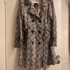 Kappa kavaj - Säljer en superchic och helt ny kappa i beige med snyggt ormskinnsmönster. 📏 På lappen står det storlek XXL, men den är mer som en M i passform – figurnära och smickrande 🐍 Tunnare material – mer som en lång kavaj än en vinterjacka 🖤 Väldigt stilren och trendig modell – passar perfekt till fest, vardag eller utekväll 🎯 Prislappen sitter kvar (dock utan angivet pris) 💯 Aldrig använd  