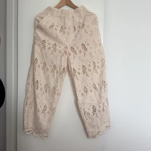 Beige byxor i broderie anglaise från HM - Beige byxor i broderie anglaise från HM. Resår i midjan och raka ben med vågig kant nertill. Två sidfickor. Halvt fodrade. 