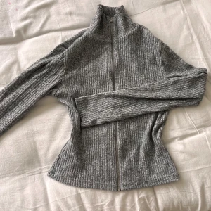 Ribbad turtleneck-kofta - Koftan är grått tyg som skiftar lite i olika nyanser, den är croppad och har hög hals. 