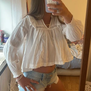 Vit blus från Gina - Superfin vit blus med volang vid axlarna och spetsdetaljer längs bröstet och ärmarna. Luftig och lite croppad modell med långa ärmar och smock vid ärmslut. Perfekt till jeansshorts eller kjol för en fräsch look. Storlek 158-164(xxs) från Gina Young💞