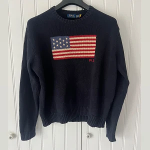 Mörkblå stickad flagg tröja Polo Ralph Lauren - Snygg mörkblå stickad tröja från Polo Ralph Lauren med amerikansk flagga framtill. Klassisk rund halsringning. Sjukt bra skick bara använd och tvättad en gång. XL men passar lätt L 