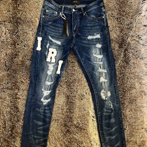 Amiri jeans blå (30) - Snygga blå jeans från Amiri med slitna detaljer och stora vita bokstavspatchar på benen. Jeansen har lite mer slim fit passform, och är i storlek 30 waist, väldigt bra material 10/10👌 Helt nytt skick med Amiri taggen. Den har klassisk femficksdesign och coolt tvättad denim. Pris kan diskuteras vid snabb affär! Tveka inte och kontakta🫡