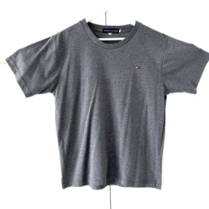 Tommy Hilfiger Stengrå-färgad t-shirt, storlek M/L - ESSENTIAL REG FIT HEATHER  StenGrå-färgad t-shirt med en liten Tommy Hilfiger-logga på bröstet. Klassisk modell med rund hals.Mycket bra kvalitet är Stor i storlek sitter som Large.  Ordpris:499kr (Se sista bilden) Bilderna togs personligen av mig, vilket säkerställer att du ser exakt den t shirten du köper.Vänligen observera att jag inte har någon öppetköp.