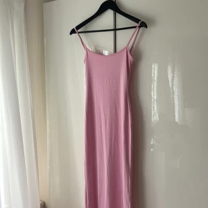 Rosa långklänning från Bershka XS - Supersöt långklänning i ljusrosa från Bershka. Klänningen har smala axelband, rak passform och ärmlös design. Perfekt för varma dagar eller när du vill ha en enkel men snygg look. Materialet känns mjukt och följsamt.