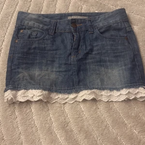 Jeanskjol med spets (pris kan redas ut) - Söt kort jeanskjol med klassiska fickor fram och bak. Kjolen har en snygg ljusblå tvätt och är dekorerad med vit spetskant längst ner för en extra gullig touch. Perfekt för dig som gillar denim med en twist!