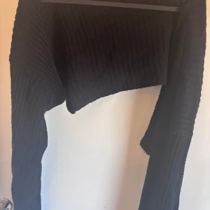 Svart croppad stickad cardigan  - Säljer en svart croppad stickad tröja med ribbad struktur. Tröjan har lång ärm och en loose passform, perfekt att styla med höga jeans eller kjol. Enkel och stilren design som funkar till många olika looks.