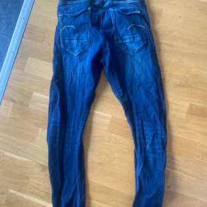 Blå jeans från G-Star RAW - Säljer ett par snygga blå jeans från G-Star RAW med klassisk femficksdesign och tydliga sömmar. Jeansen har normal passform och är tillverkade i slitstarkt bomullsdenim. Perfekta för dig som gillar en stilren och tidlös look. Storlek 29/32. 