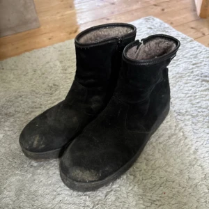Svarta vinterboots från McKinley - Svarta boots från McKinley med mjukt pälsfoder på insidan. Yttermaterialet är mocka och de har dragkedja på sidan för enkel påtagning. Perfekta för kalla dagar med sin varma och sköna insida. Klassisk rund tå och platt sula.