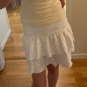Vit volangkjol - Supersöt vit kortkjol med volanger och broderade detaljer. Kjolen har smock i midjan för en bekväm passform och är gjord i luftigt material, perfekt för varma dagar. Den har ett romantiskt och somrigt uttryck som är lätt att matcha. Storlek 134/140 men passar även mig som är 164cm pga den stretchiga midjan 🥰skriv vid funderingar