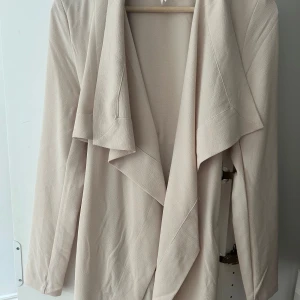 Beige trenchcoat med knytband - Snygg beige trenchcoat med långa ärmar och breda slag. Jackan har ett knytband i midjan och en knappdetalj bak. Perfekt för dig som gillar stilrena och enkla plagg med en modern touch.