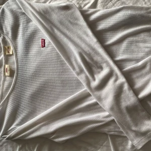 Kläder - Vit långärmad tröja från Levi's i ribbad bomull med rund hals och diskret röd logotyp på bröstet. Enkel och clean stil som funkar till allt, perfekt för lager-på-lager eller solo. Sitter skönt och har en klassisk passform. En vit tunn cardigan. En T-shirt med snygga hål. 75kr för Levi’s tröjan och 50kr för resten styck. Alla tillsammans för 150kr