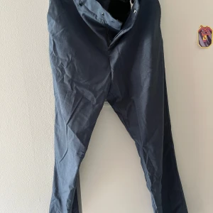 Mörkblå kostymbyxor med raka ben - Snygga mörkblå kostymbyxor med klassisk passform och raka ben. Byxorna har hällor för bälte, diskreta bakfickor och stängs med knapp och dragkedja. Perfekta för en clean och stilren look.