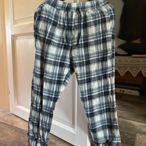 Rutiga mjukisbyxor från Mywear Woman - Mysiga rutiga mjukisbyxor från Mywear Woman i blått och vitt. Byxorna har resår och snörning i midjan för skön passform. Perfekta för chill hemma eller som pyjamasbyxor. Tillverkade i mjukt bomullstyg.