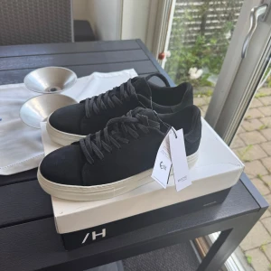 Svarta sneakers från Selected Homme - Stilrena svarta sneakers från Selected Homme med vit platt sula och klassisk snörning. Ovandelen är i mocka för en lyxig känsla och skon har en rund tå. Perfekta för dig som gillar minimalistisk och clean stil.