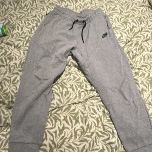 Grå mjukisbyxor från Nike XL - Snygga grå mjukisbyxor från Nike i storlek XL. Byxorna har resår och snörning i midjan, två sidofickor och Nike-logga på låret. Perfekta för chill eller träning, tillverkade i mjukt bomullsmaterial.