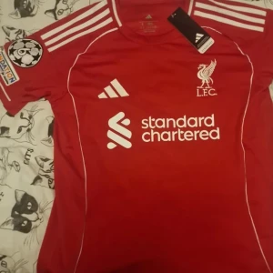 Liverpool röd matchtröja Adidas Wirtz 11 - Röd Liverpool fotbollströja från Adidas med vita detaljer, klubbmärke och sponsortryck framtill. Nummer 11 och namnet Wirtz på ryggen, Champions League-märke på ärmen och klassiska Adidas-ränder på axlarna. Tillverkad i lätt och ventilerande material.