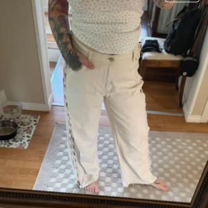 Beiga wide jeans med snörning i sidan - Säljer ett par beiga jeans med breda ben och snygg snörning längs båda sidorna. Hög midja och råa kanter nertill ger en cool vibe. Perfekta för dig som vill sticka ut lite extra. Materialet är kraftig bomullsdenim. Avklippta 
