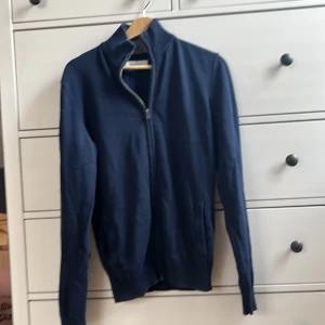 Mörkblå cardigan med dragkedja - Mörkblå cardigan jacka från pier one med hel dragkedja framtill och hög krage. Tröjan är i mjukt bomullsmaterial, har två fickor och ribbade muddar vid ärmslut och nederkant. Perfekt för dig som gillar en clean och stilren look.