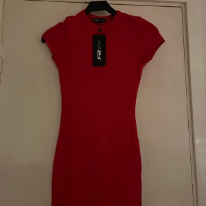 Röd kortklänning från FB Sister - Säljer en snygg röd kortklänning från FB Sister. Klänningen har en enkel och tight passform med korta ärmar och rund halsringning. Perfekt för dig som gillar en stilren look med färg. 