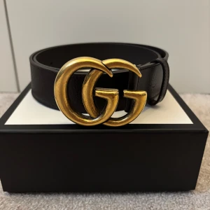 Gucci GG Marmont Brown Belt Unisex Size 40 Dollar Pigprint  - Säljer ett mycket snyggt designer bälte från Gucci. Bältet är brunt, 40 mm bred och i storlek 90 (Gucci 90). Endast använd 3 ggr vid speciella tillfällen. Väldigt varsamt använd, som ny. Med bältet medföljer identifikation, ”controllato”, dustbag, original kartong med streckkod, mindre tygpåse, presentsnörning. Inköpt på Gucci Europe hemsida år 2020.  Kvitto för äkthet finns vid begäran. Pris 2020: €320 (3 545 SEK) , Nypris 2025 : SEK 5 300.
