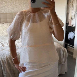 Ljusrosa blus med puffärm - Superfin ljusrosa blus med transparent tyg och små prickar i strukturen. Blusen har puffiga korta ärmar och rund halsringning, perfekt för en söt och trendig look. Lätt och luftig känsla, passar perfekt till kjol eller jeans.