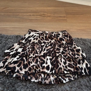 Leopardmönstrad volangkjol - Snygg kort kjol med leopardmönster och flera volanger. Kjolen har en cool och trendig look. Färgerna går i beige, brun och svart. Passformen är normal och materialet känns lätt och följsamt.