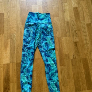 Blå-gröna tränings tights  med bladprint & fickor  - Snygga tränings tights med fickor längs benen & tropiskt bladmönster i blått och grönt. Hög midja och stretchigt material som sitter skönt på kroppen. Perfekta för träning eller chill dagar när du vill sticka ut lite extra.