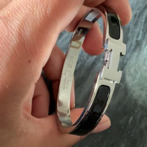 Harmens svart och silver armband - Snyggt armband från Harmens i silverfärgad metall med svarta detaljer och ikoniskt H-spänne. Stilren och modern design som verkligen sticker ut på handleden. Perfekt accessoar för dig som gillar lyxiga och tidlösa smycken.