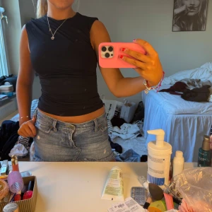 Svart ärmlös croppad topp - Säljer en svart, tight och croppad ärmlös topp med rund hals. Sitter snyggt figurnära och är perfekt till jeans eller kjol. Enkel och stilren design som är lätt att matcha. Materialet känns stretchigt och bekvämt.