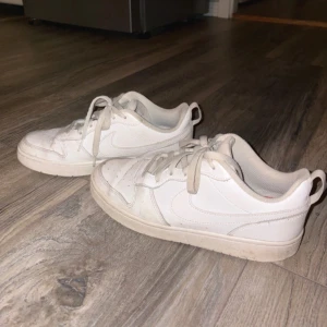 Vita Nike sneakers med snörning - Klassiska vita Nike sneakers i skinn med låg profil och rund tå. Skorna har snörning och diskret Nike-logga på sidorna. Perfekta för en clean och sportig look. 