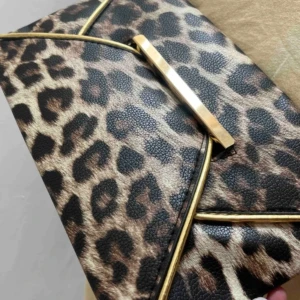 Leopardmönstrad kuvertväska med gulddetaljer - Snygg kuvertväska i leopardmönstrat syntetmaterial med guldfärgade metalldetaljer. Väskan är 28x18 cm och har ett stilrent svart foder. Perfekt accessoar.