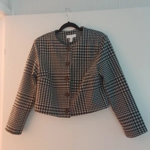 Rutig svartvit overshirt från H&M - Stilren overshirt från H&M i svartvitt rutigt mönster. Jackan har rund halsringning, stora svarta knappar framtill och är croppad i modellen. Har långa ärmar. Perfekt för lager-på-lager och snygg till jeans.