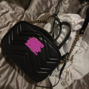 Svart quiltad axelväska med kedja - Säljer en svart quiltad axelväska med klassiskt GG-mönster. Väskan har guldfärgad kedja och dragkedja, samt justerbar axelrem i skinn. Perfekt storlek för det viktigaste och riktigt snygg till alla outfits.