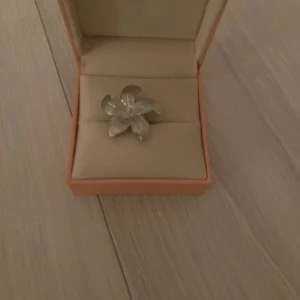 Blommig silverring i unik design - Säljer en snygg ring i form av en blomma, tillverkad i silverfärgat material. Ringen har fem tydliga blomblad och en cool, lite chunky känsla. Perfekt för dig som vill sticka ut med ett smycke som känns både trendigt och personligt.