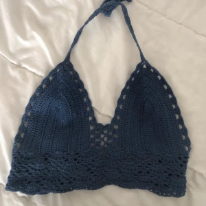 Blå virkad topp  - Superfin blå virkad topp med knyt i nacken och ryggen. Toppen har trekantsformade kupor och snygga håldetaljer längs kanterna. Perfekt för sommardagar och festivaler.