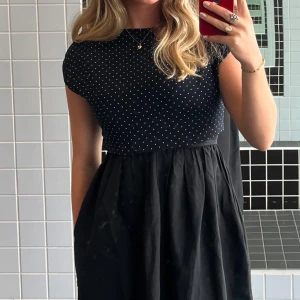 Svart croppad blus med vita prickar - Säljer en svart croppad blus med små vita prickar. Toppen har korta ärmar och resår i nederkanten för en snygg passform. Perfekt till jeans eller kjol för en trendig look.